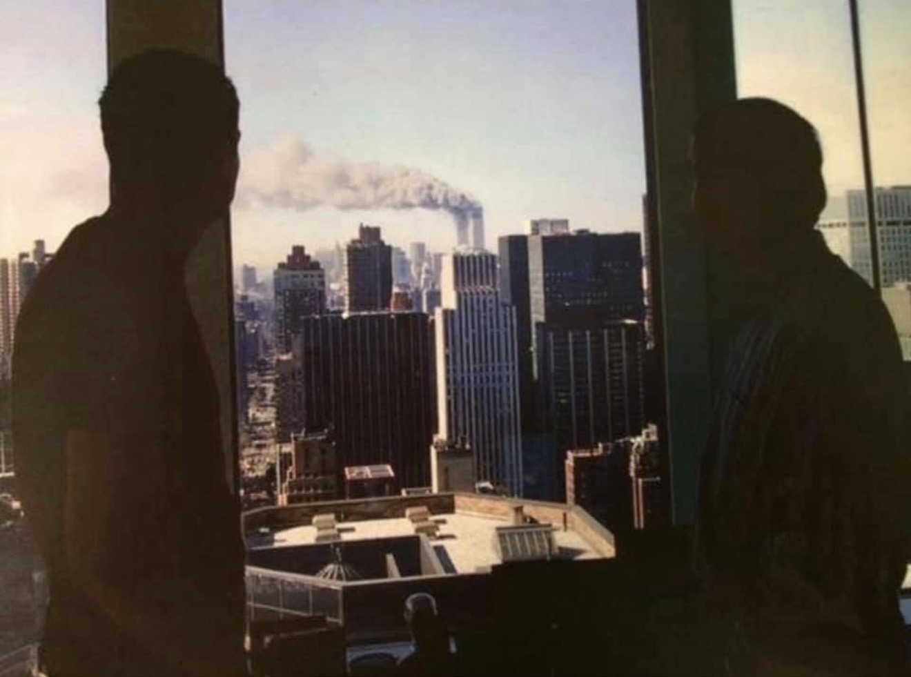 Two men in silhouette at an office window, looking south toward smoke rising over lower Manhattan